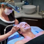 The image shows a smiling client receiving an Aqua Pure Facial, a 3-in-1 treatment for cleansing, hydrating, and rejuvenating the skin.